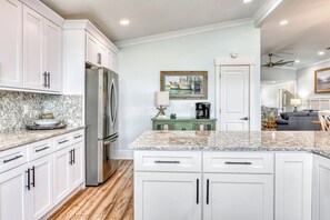 A modern kitchen with white cabinets, a stainless steel refrigerator, and a marble countertop.