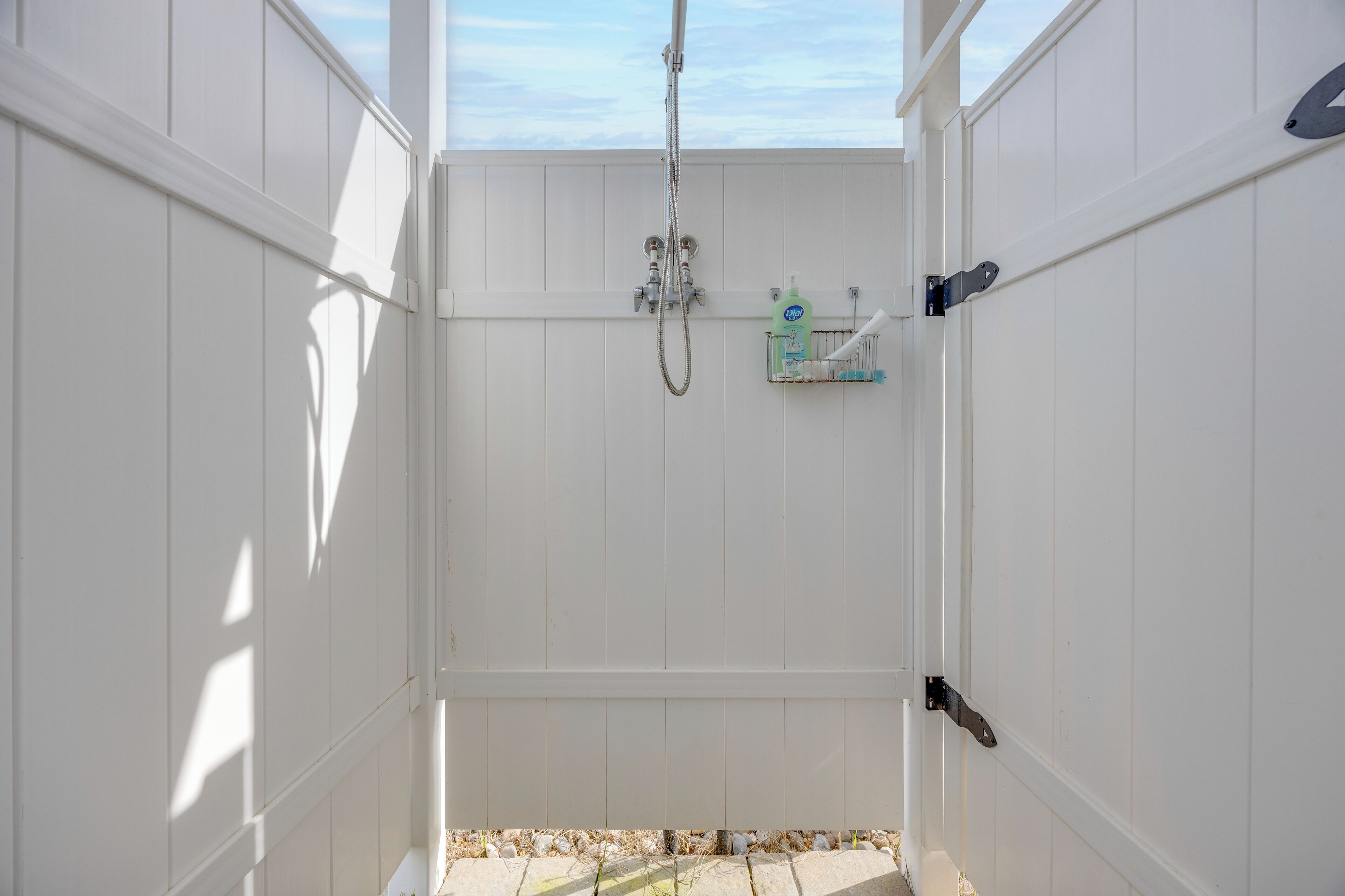 Een witte badkamer met een douche, een handdoekhouder en een zeepdispenser.