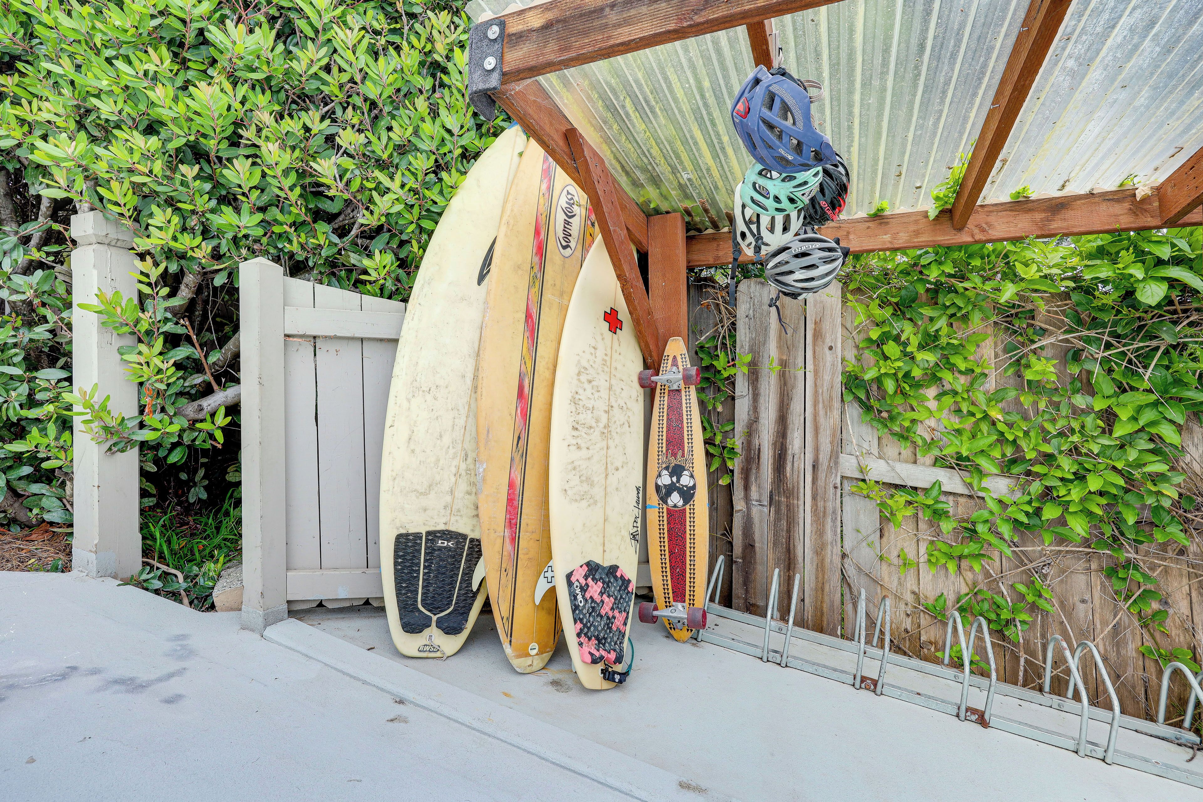 Une structure en bois, avec des planches de surf appuyées contre, un casque suspendu sur le côté et un présentoir métallique sur roulettes.