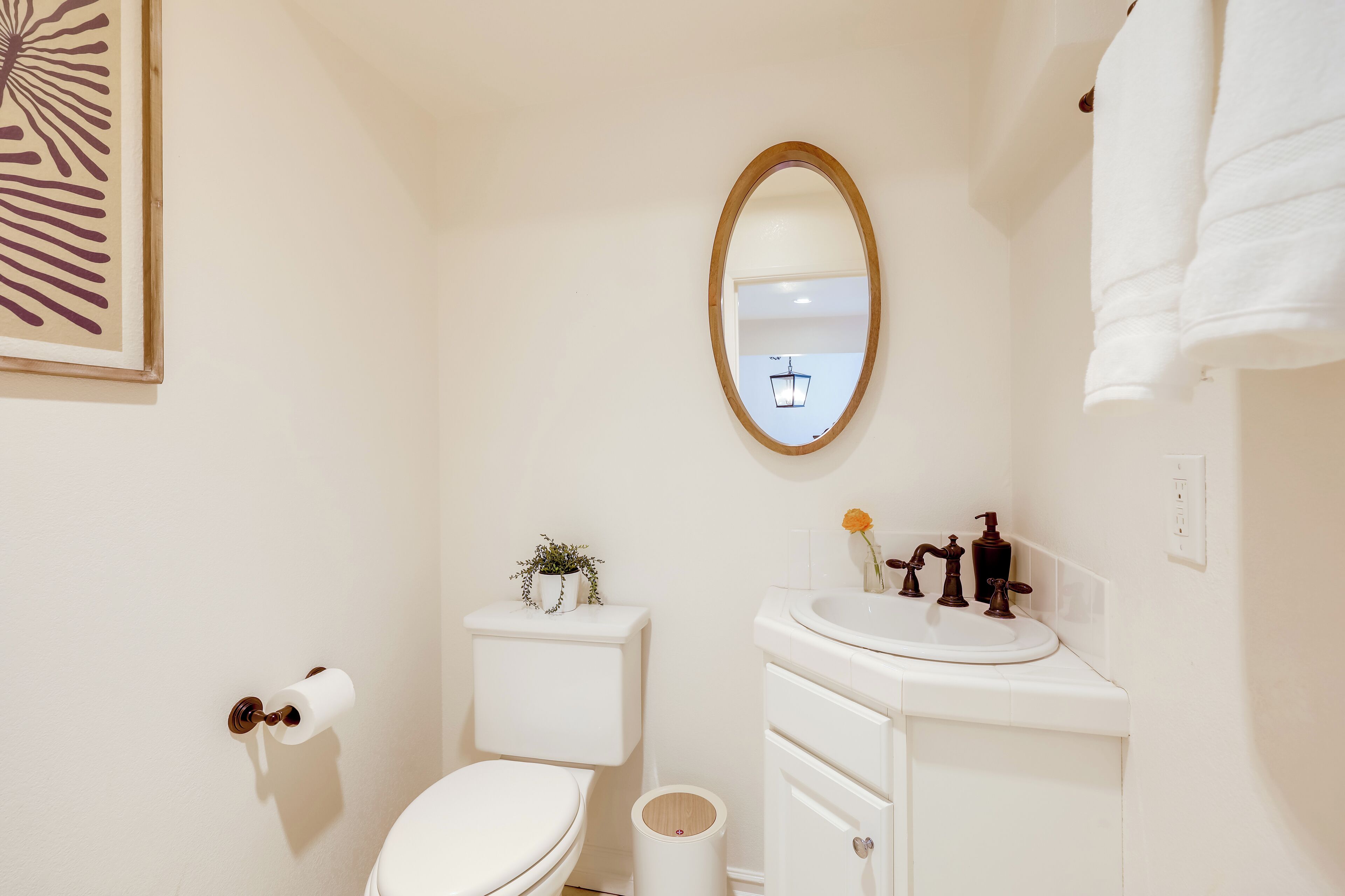 A bathroom with a toilet, sink, mirror, and a framed artwork on the wall.