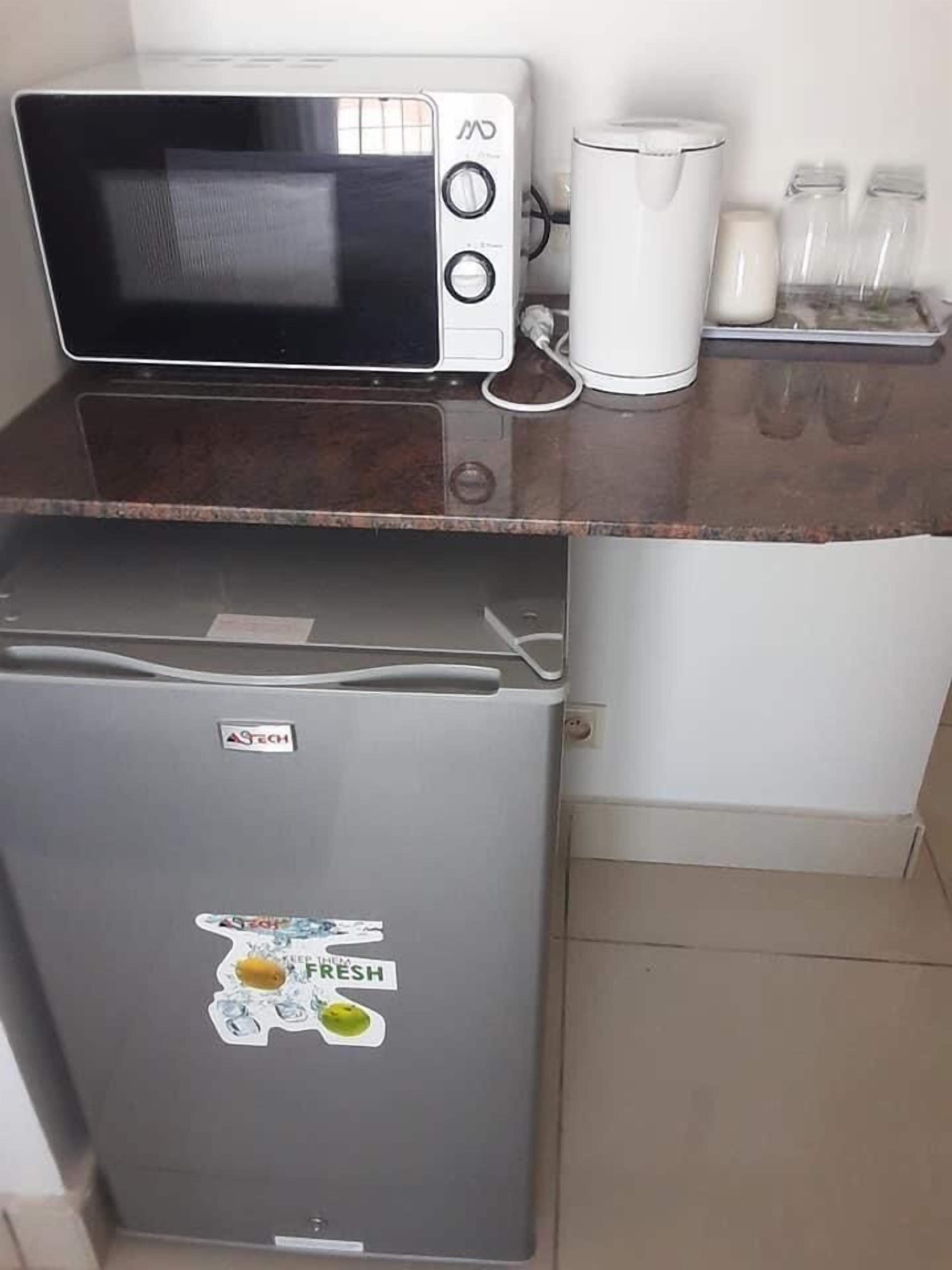 Een kitchenette met een magnetron, een kleine koelkast en een koffiezetapparaat op een aanrecht.
