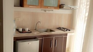 A compact kitchen with a refrigerator, sink, and wooden cabinets. - Résidence Mad 75 (Dakar)