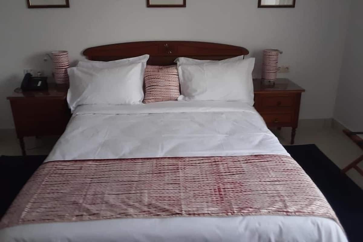 A neatly made bed with white bedding and a pink and white striped blanket. There are two bedside tables with lamps and a framed picture on the wall above the bed.
