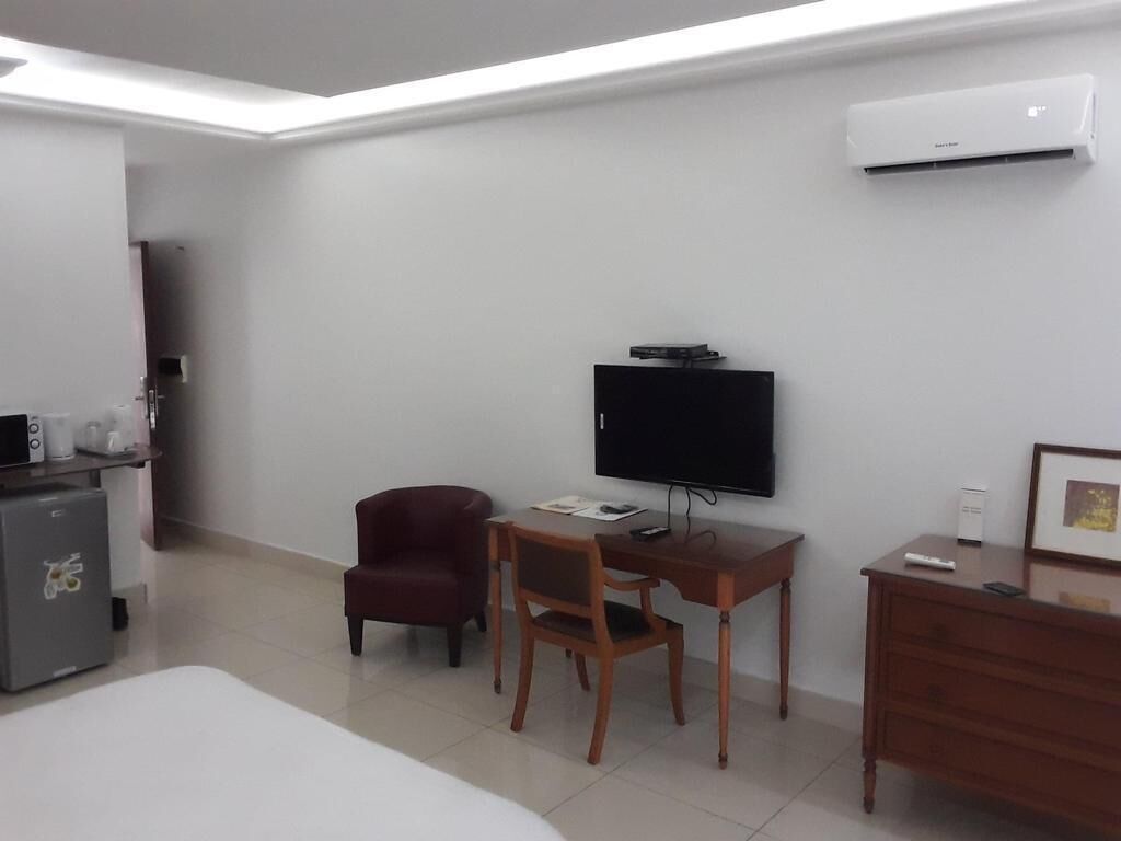 Habitación de hotel con cama, escritorio con silla, televisor, cómoda y unidad de aire acondicionado en la pared.
