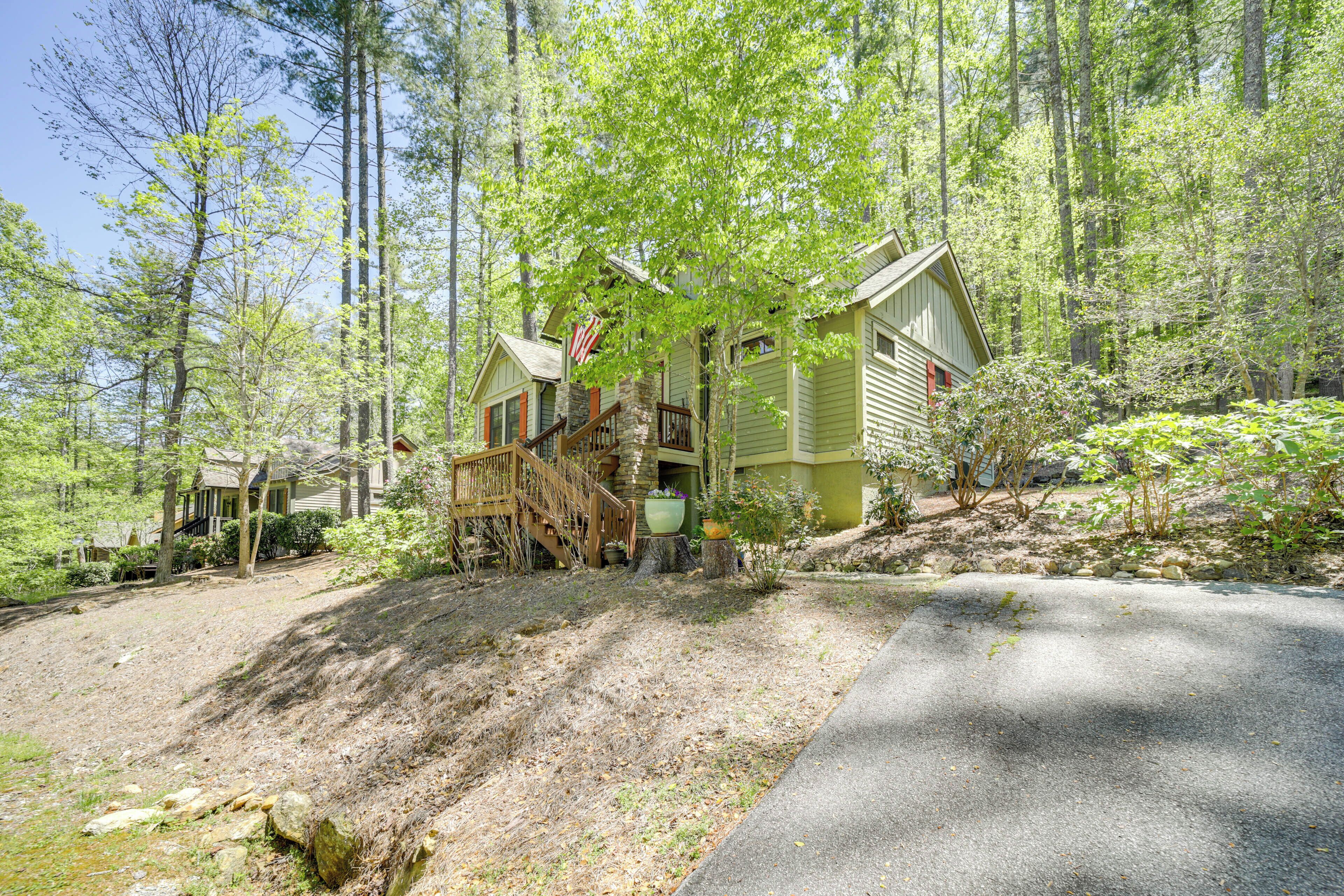 Une maison à deux étages avec un escalier en pierre menant à une terrasse en bois, le tout entouré d’une zone boisée.