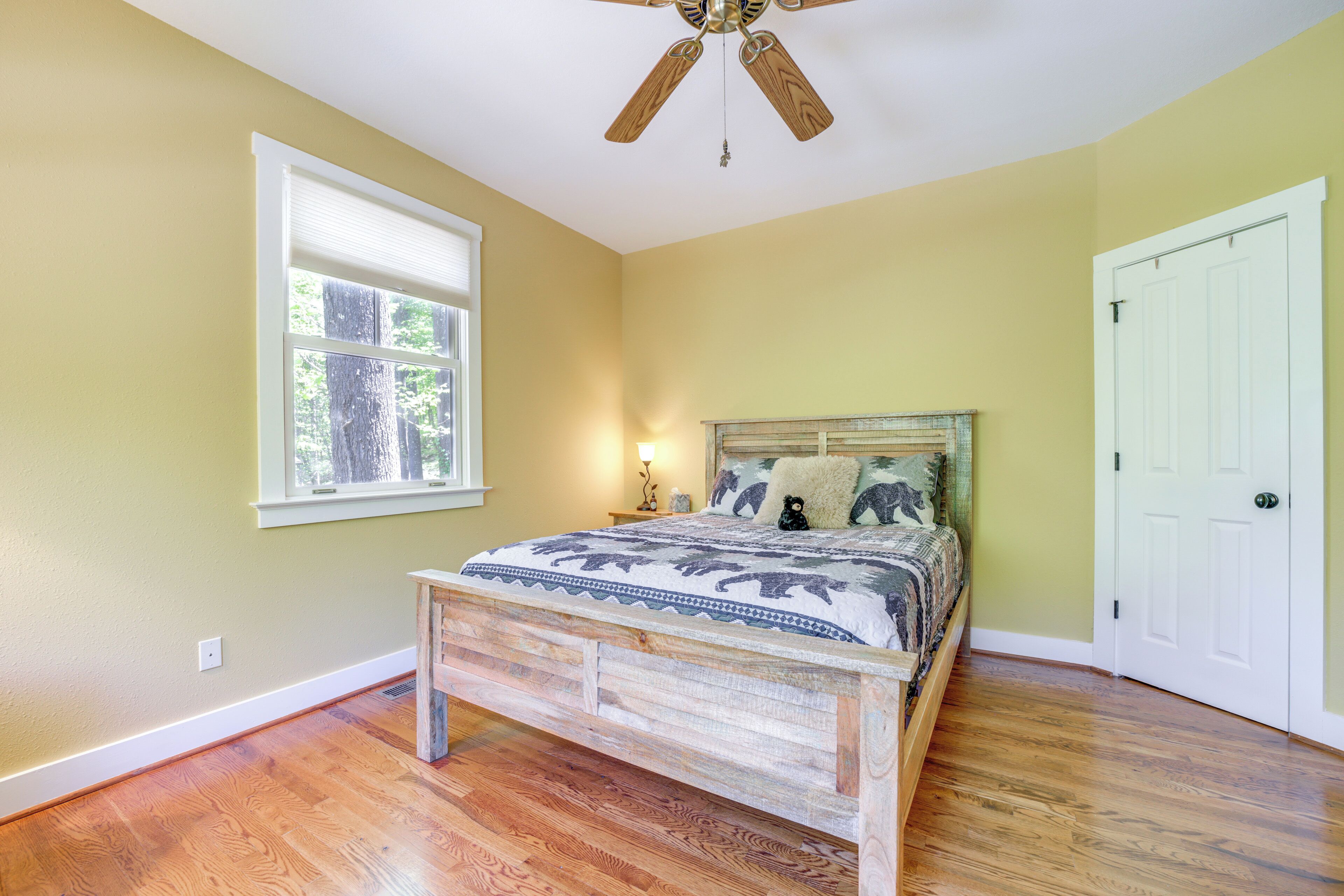A bedroom with a wooden bed, a ceiling fan, a window with blinds, and a white door.