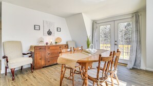 A dining area with a wooden table and chairs, a wooden cabinet, and a view of the outdoors through a glass door. - Charming Maine Retreat Near Skiing & ATV Park! (Dixfield)