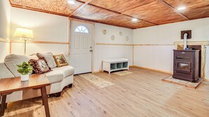 A cozy living room with a wooden ceiling, a white door, a sofa with cushions, a small table with a plant, and a wood-burning stove. - Charming Maine Retreat Near Skiing & ATV Park! (Dixfield)