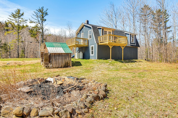 Ein zweistöckiges Haus mit einer Holzterrasse und einem kleinen Gartenhaus.