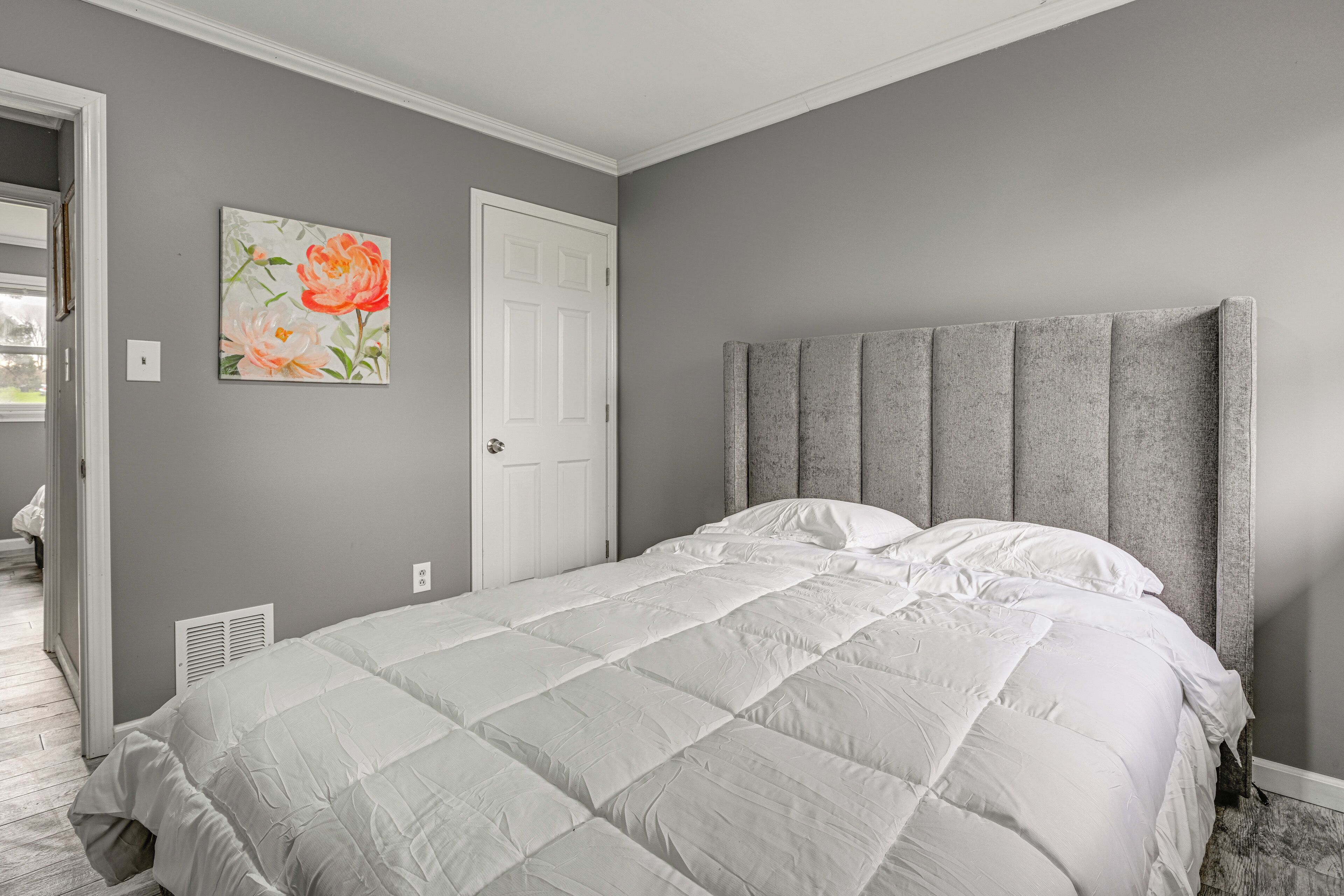 A bedroom with a large bed, a grey headboard, and a door.