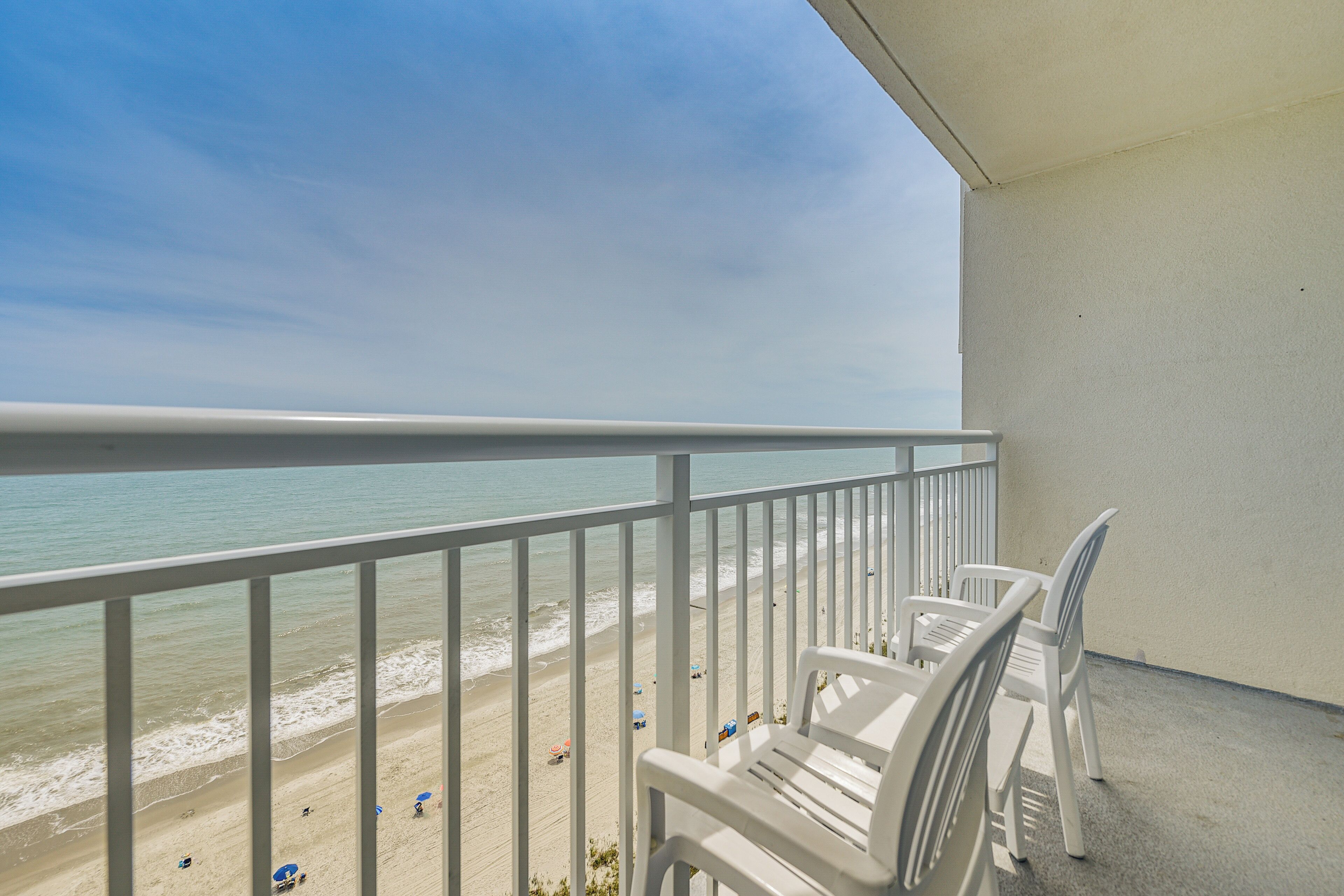 A balcony with white chairs overlooking a beach.