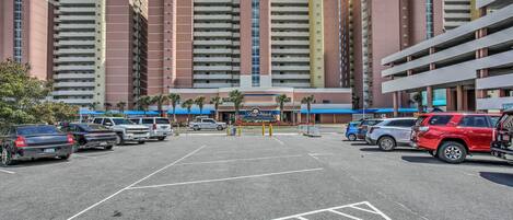 A parking lot with multiple cars and a building with a central tower and multiple balconies in the background.