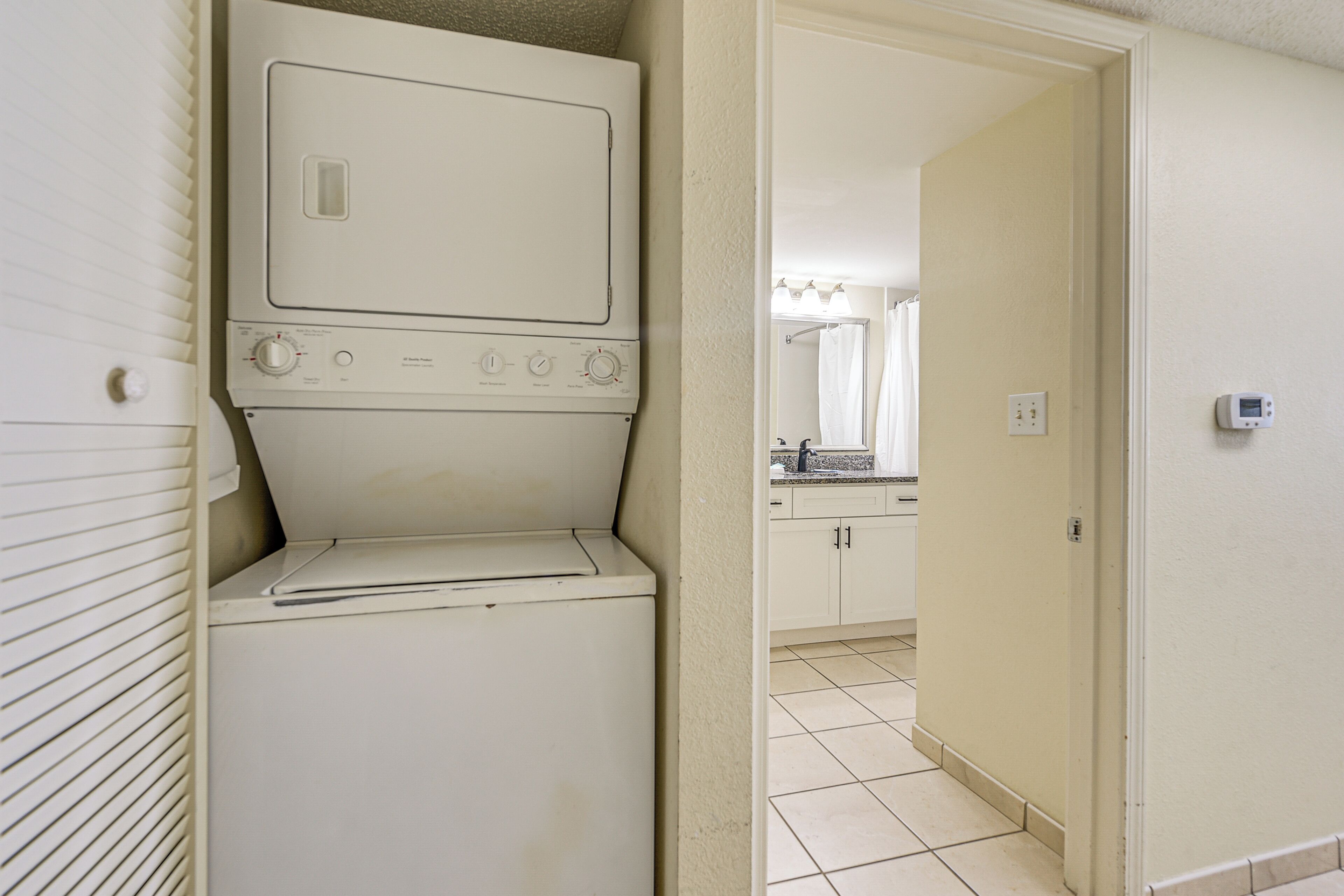 A laundry room with a washer and dryer, a bathroom with a shower, and a kitchen area with a sink and cabinets.