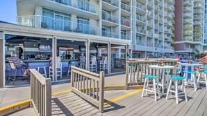 A deck area with outdoor seating, a bar, and a view of a multi-story building with balconies. - Walk to Beach: North Myrtle Beach Resort Apt! (North Myrtle Beach)
