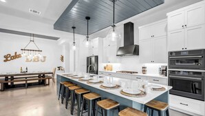 Een moderne keuken met een centraal eiland, barkrukken, witte kastjes en hanglampen.