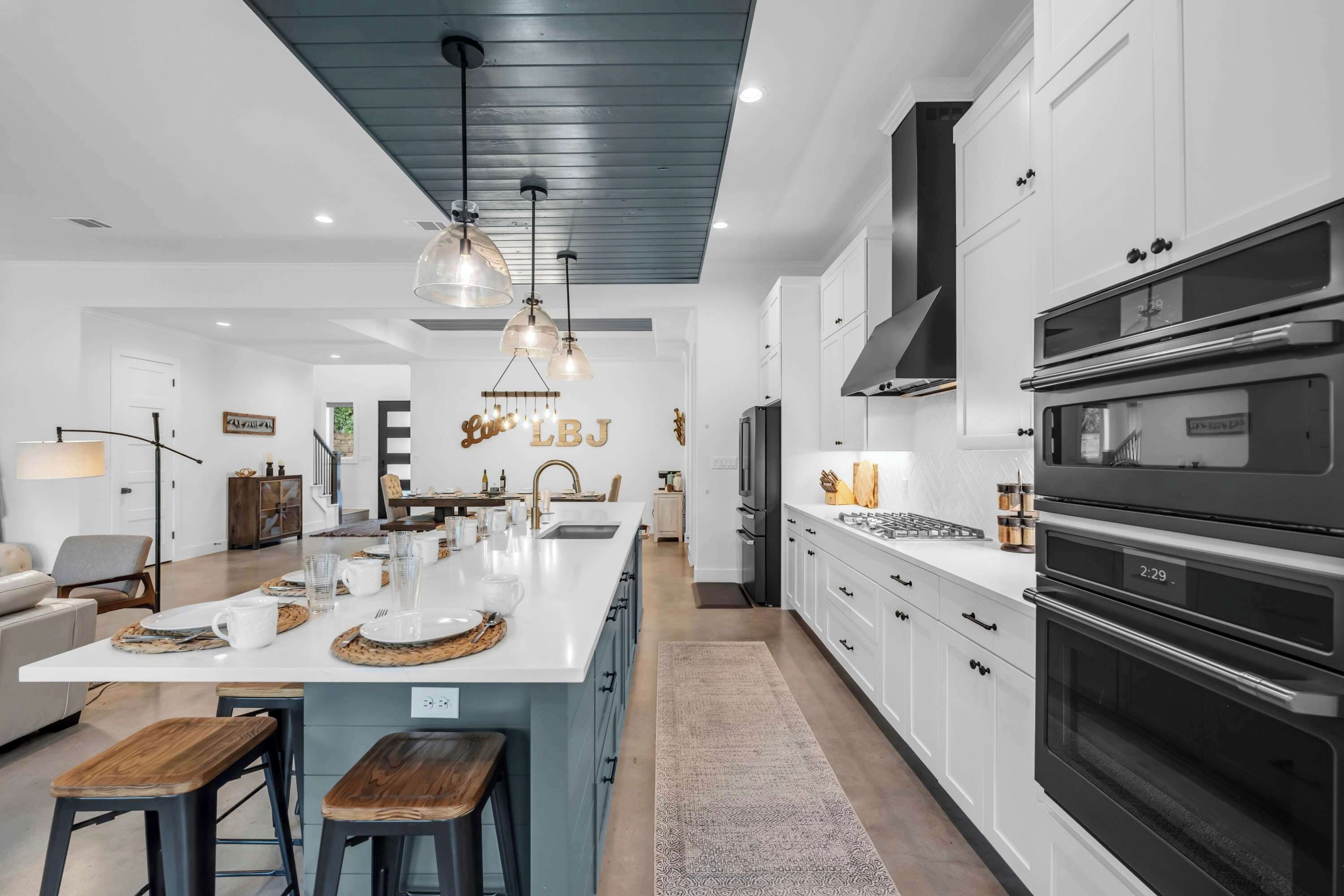 A modern kitchen with white cabinets, a large island, pendant lighting, and a built-in oven.