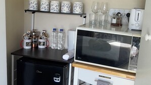 A compact kitchenette with a refrigerator, microwave, and a small shelf with tea kettles and glasses. - Mel’s Retreat - Private Room & Ensuite (Te Kuiti)