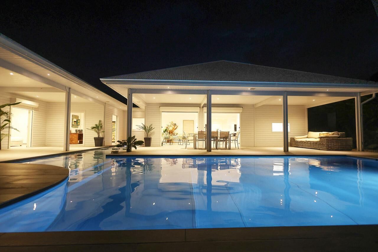A modern house with a swimming pool, large glass doors leading to a patio, and a well-lit interior.