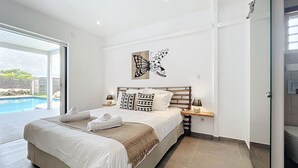 A bedroom with a large bed, a nightstand, a wall-mounted lamp, and a butterfly art piece. - Nakolodge 4 chambres - piscine / balneo / jardin privatifs  (Sainte-Anne)