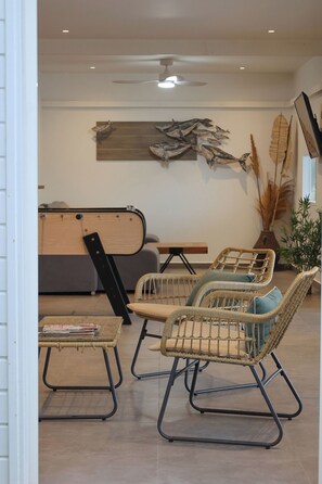 A modern living room with wicker furniture, a ceiling fan, and decorative wall art. - Nakolodge 4 chambres - piscine / balneo / jardin privatifs  (Sainte-Anne)