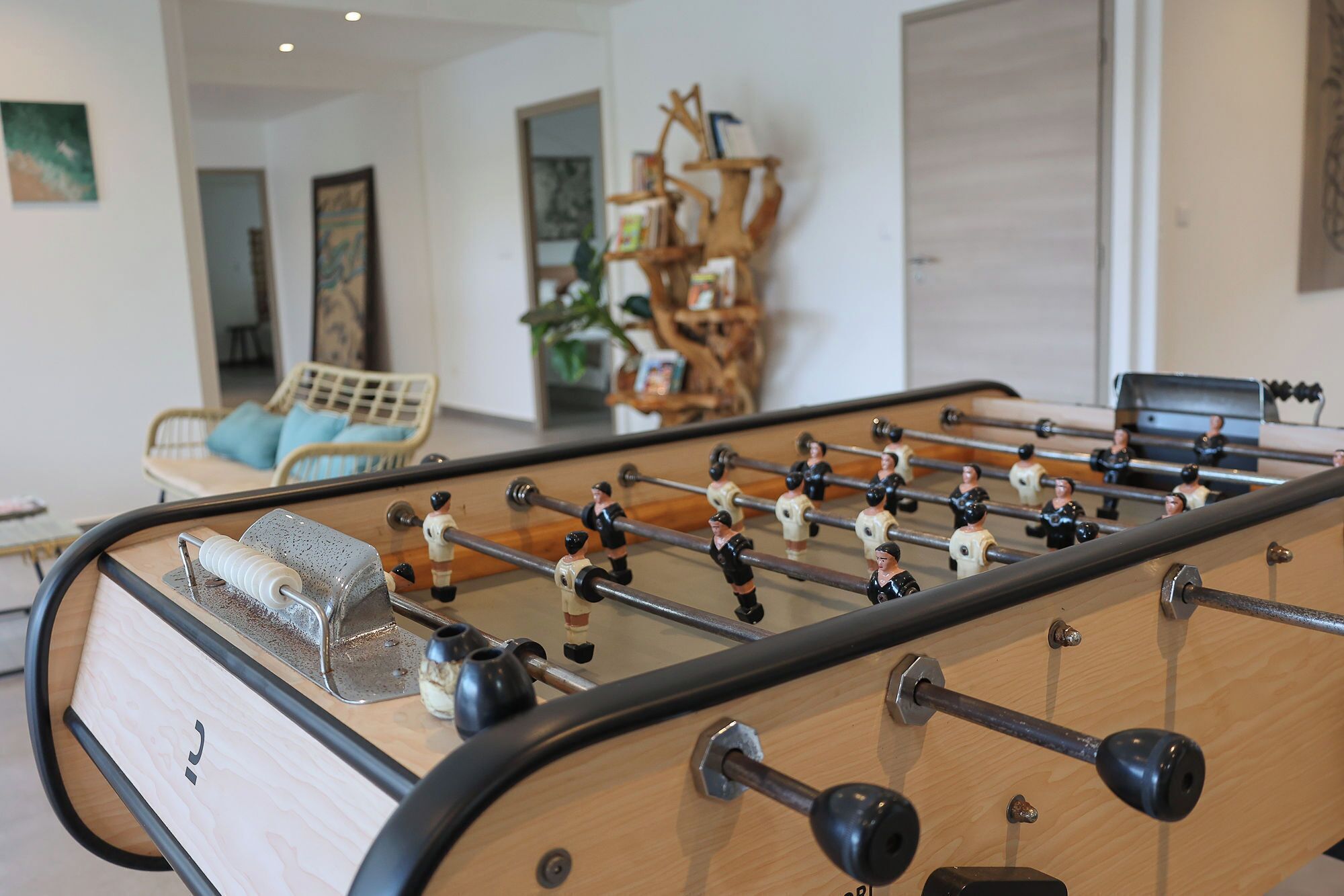 A foosball table in a room with a wicker chair and a wooden cabinet with books.