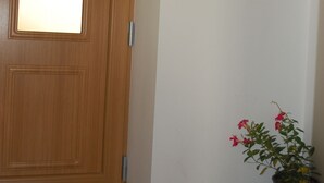 Une porte en bois avec une fenêtre, une plante en pot aux fleurs rouges et un plancher en bois.