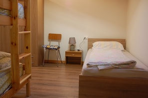 A bedroom with a wooden bunk bed, a single bed, a nightstand with a lamp, and a chair. - COZY AND SPACIOUS ALPINE ATTIC ROOM WITH PETS ALLOWED (Alleghe)
