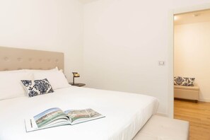 A neatly arranged bedroom with a bed, pillows, a bedside table with a lamp, and a book on the bed.