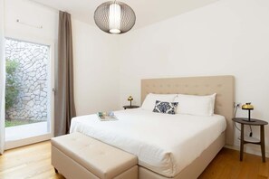A bedroom with a bed, bedside tables, a lamp, a window with curtains, and a view of greenery.