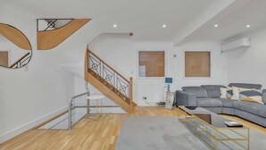 A modern living room with a staircase, a grey sofa, and a glass coffee table. - Family Town-House Behind Park Lane (London)