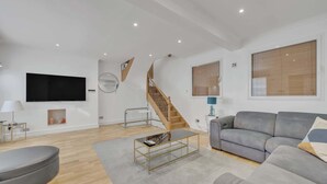 A modern living room with a staircase, a flat-screen TV, and a grey sofa. - Family Town-House Behind Park Lane (London)