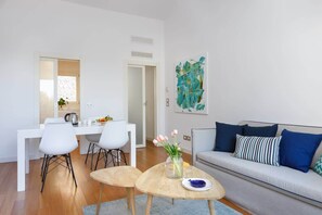 A modern living room with a sofa, a dining table with chairs, and a kitchen area.