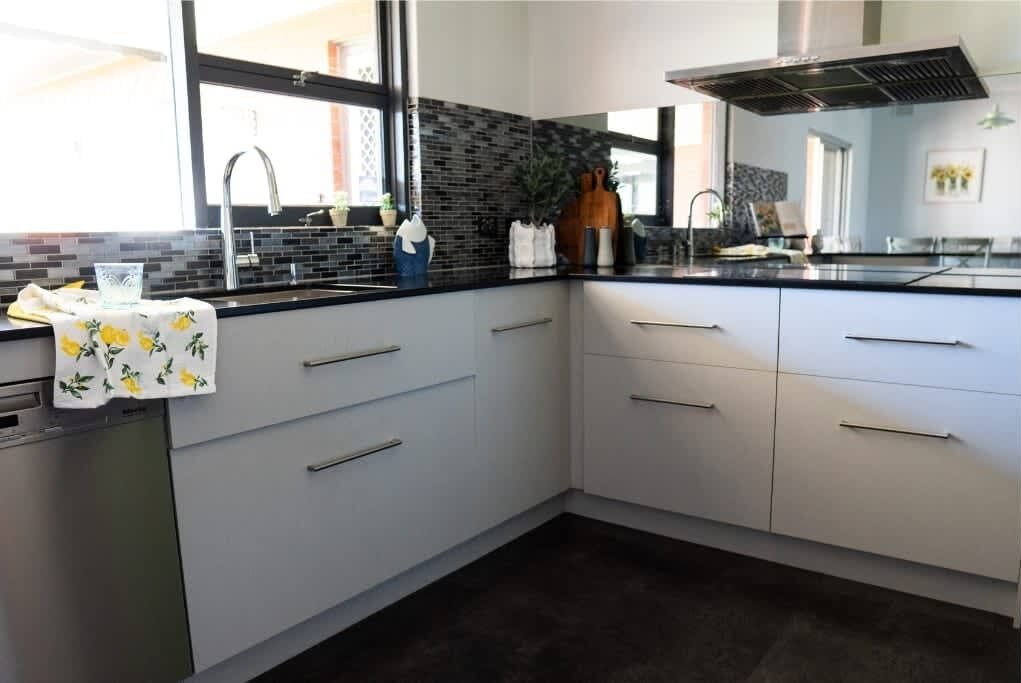 A modern kitchen with a black countertop, white cabinets, a stainless steel sink, and a window providing natural light.