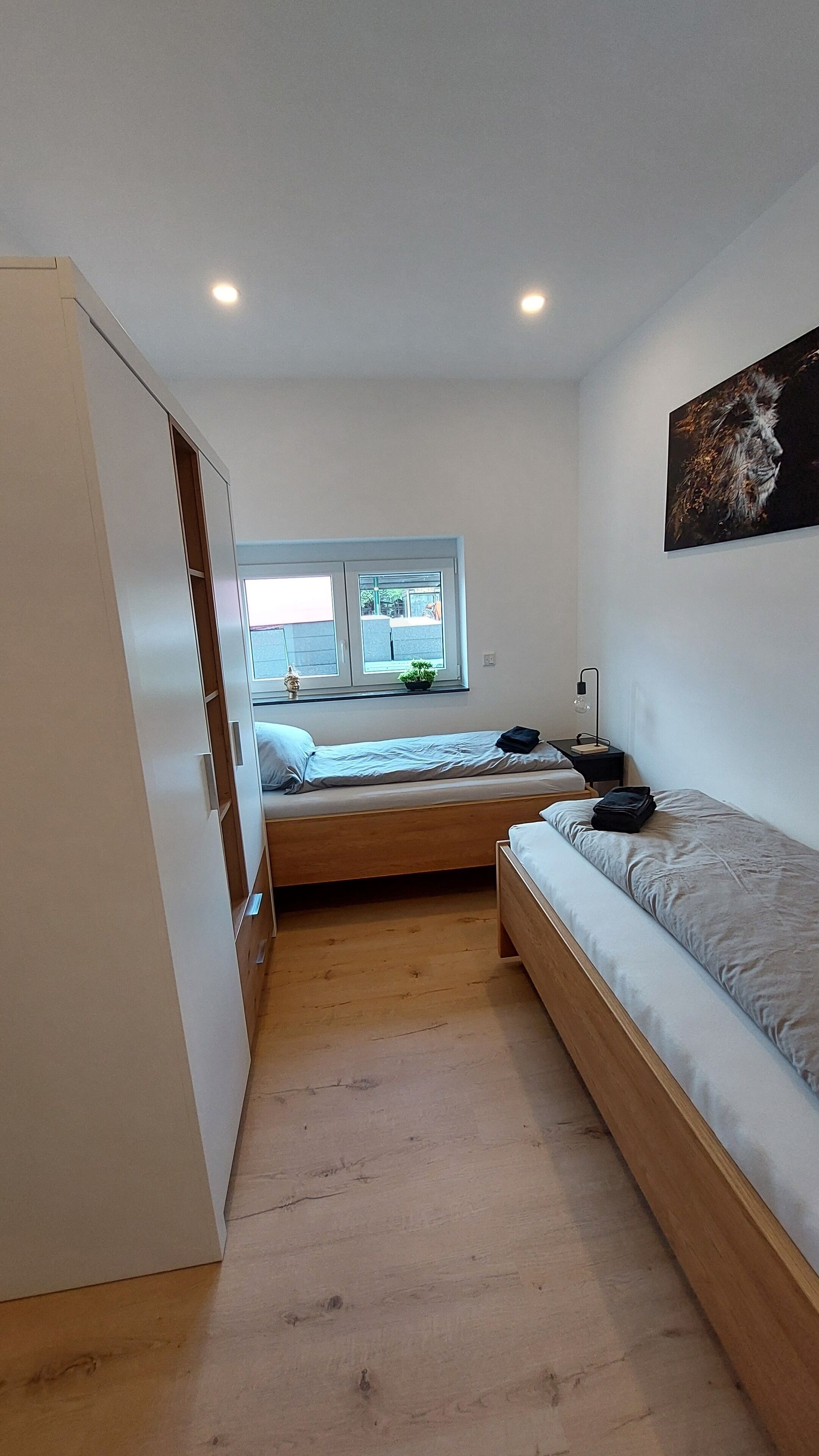 A compact bedroom with a single bed, a small desk, and a window with a view of the outside.