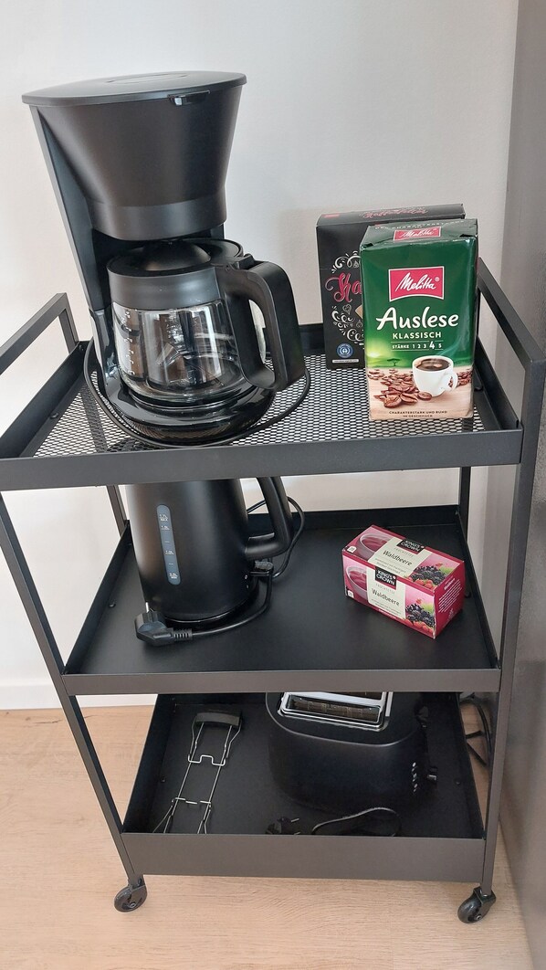 A coffee maker on a metal cart with two boxes of coffee and a coffee pod.