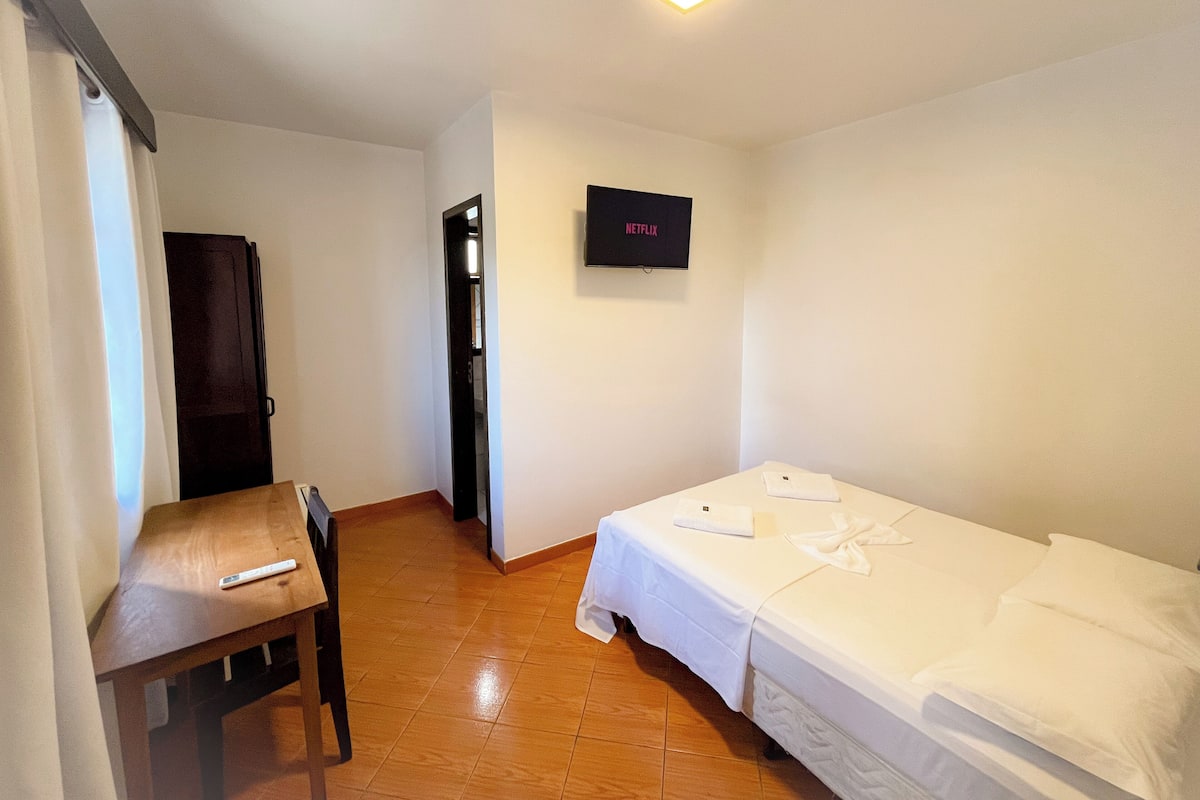 Ein Hotelzimmer mit Bett, Schreibtisch, Stuhl, Fernseher und Tür.