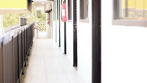 A corridor with a tiled floor, a metal railing on one side, and a door with a black frame on the other. - Hotel Vandressen & Castro (Garuva)