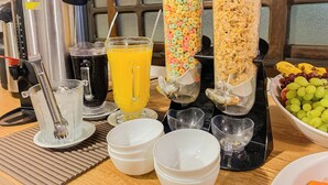 A breakfast buffet setup with cereal dispensers, a juice dispenser, and a bowl of grapes. - Hotel Vandressen & Castro (Garuva)