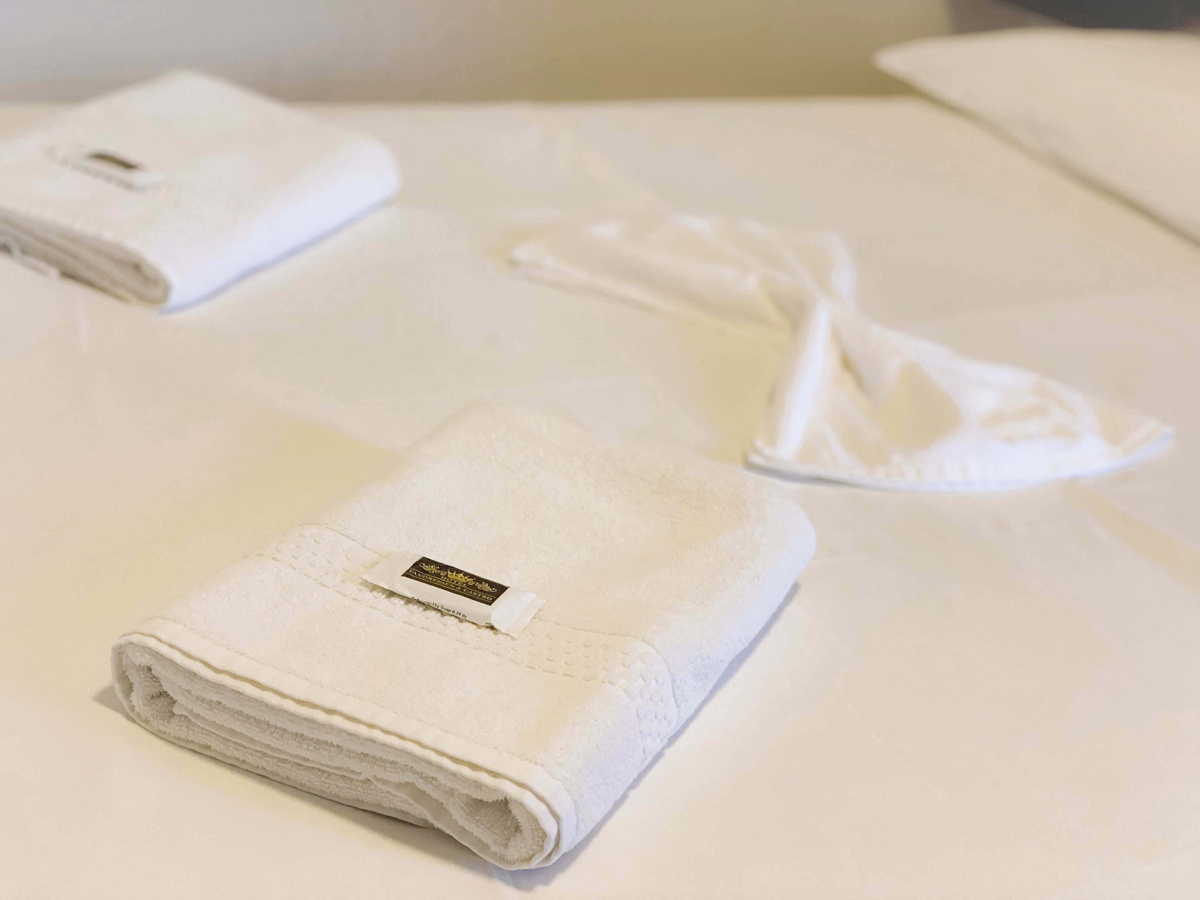 Ein ordentlich bezogenes Bett mit einem gefalteten weißen Handtuch und einem ordentlich gefalteten weißen Bademantel darauf.