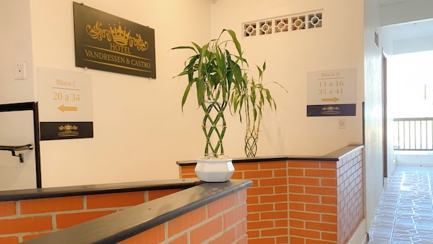 A hotel reception area with a brick counter, directional signs for blocks C and B, and a potted plant. - Hotel Vandressen & Castro (Garuva)