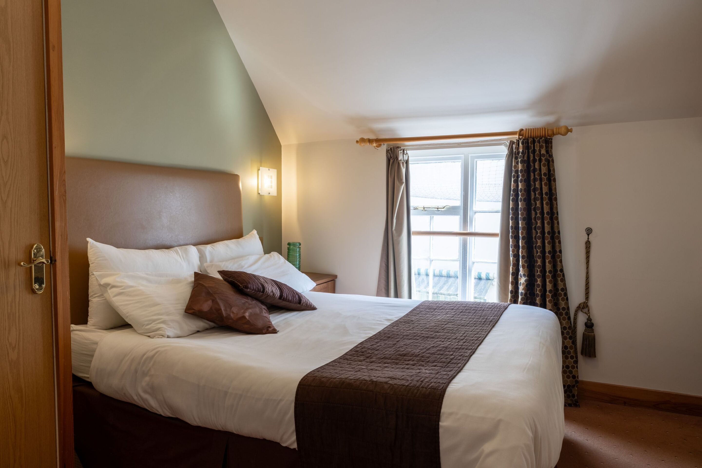 A neatly made bed with white and brown bedding, a wooden headboard, and a bedside table with a green bottle.