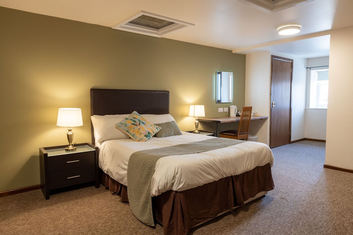 A bedroom with a bed, nightstands, a desk, and a chair.