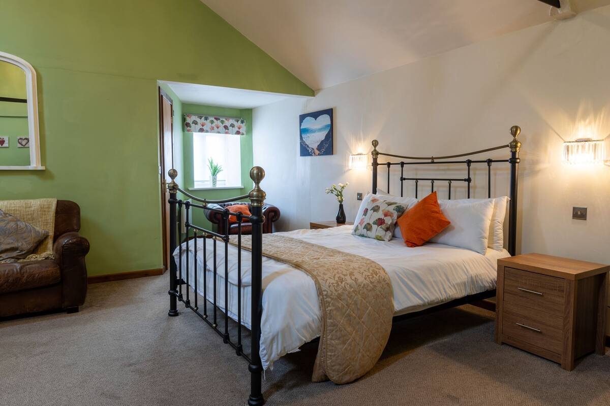 A bedroom with a bed, a nightstand, a dresser, a window with a view, and a green wall.