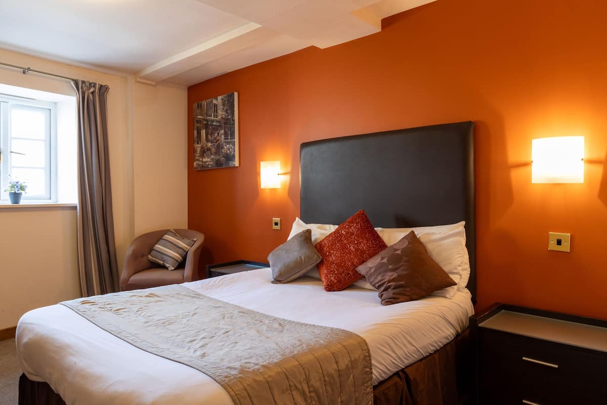 A hotel room with a large bed, two bedside tables, a chair, and a window with curtains.