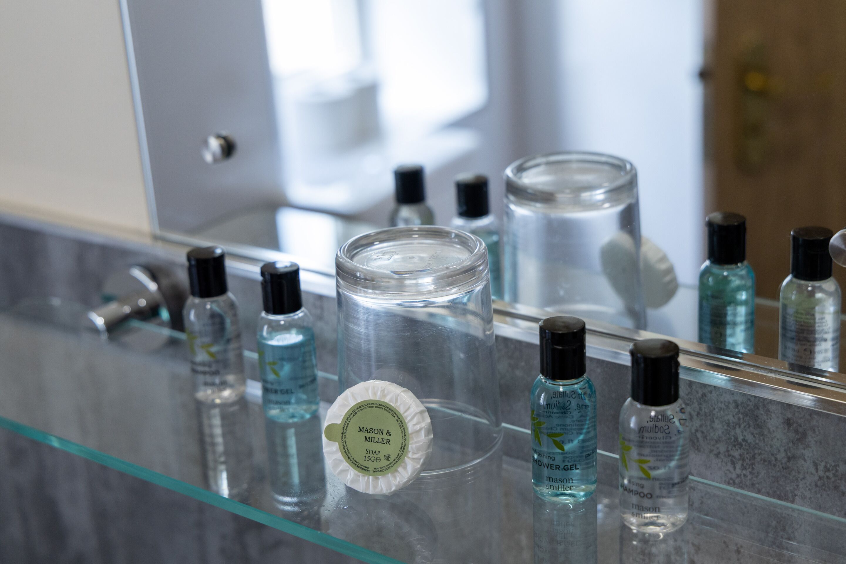 Una encimera de baño con diferentes artículos de aseo, incluyendo una pastilla de jabón, champú y gel de ducha.