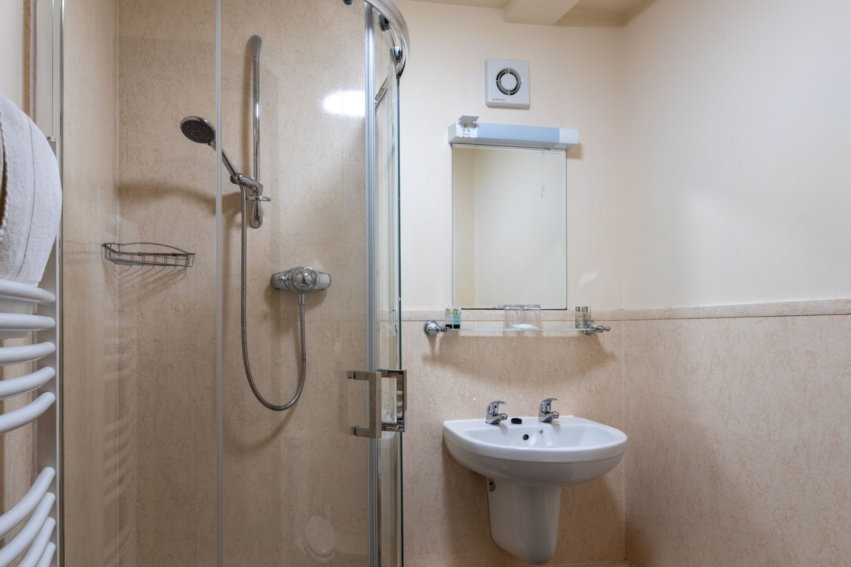 Un baño con ducha compartimentada por vidrio, un lavabo blanco y un perchero para toallas.