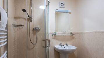 Un baño con ducha compartimentada por vidrio, un lavabo blanco y un perchero para toallas.