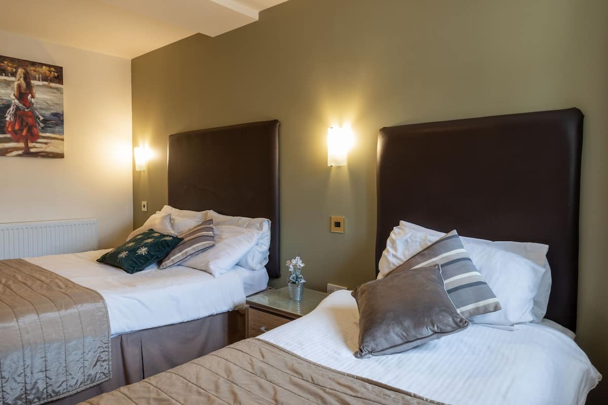 A hotel room with two beds, each with a headboard, bedside tables, and lamps.