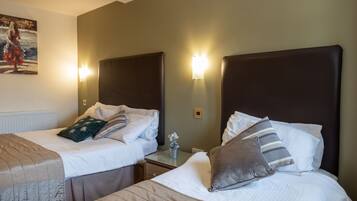 A hotel room with two beds, each with a headboard, bedside tables, and lamps.