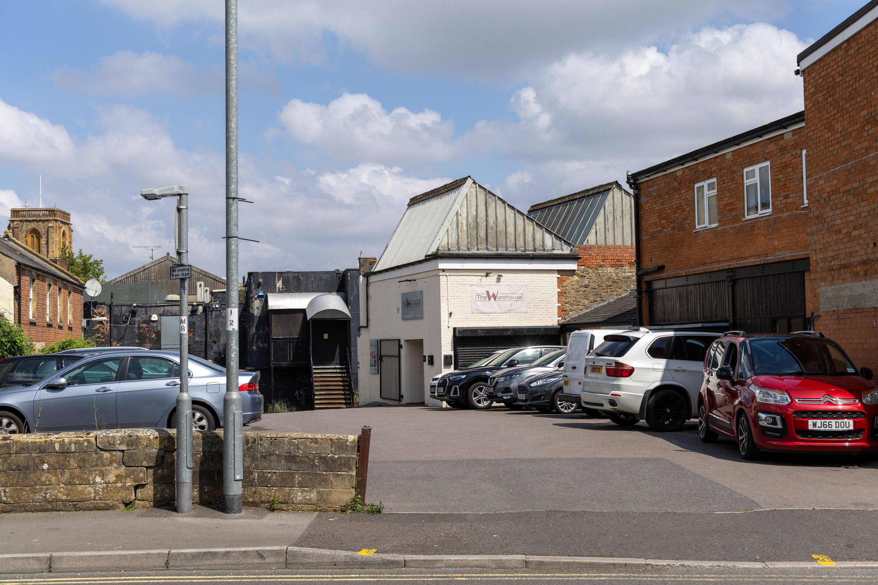 A street view with parked cars, a building labeled "The Warehouse," and a brick building with a chimney.